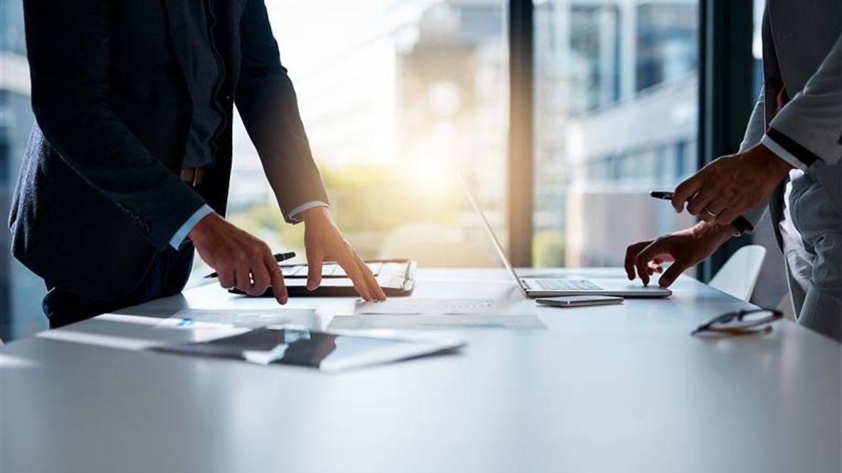 Zwei Mitarbeitende bearbeiten Dokumente an einem Schreibtisch 